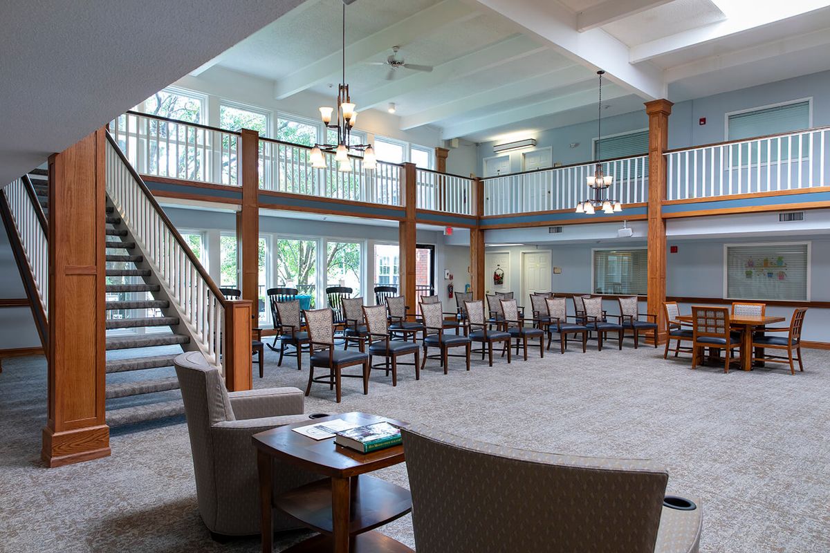 A spacious room with multiple chairs arranged in a seating area, featuring a staircase and large windows that allow natural light to fill the space.