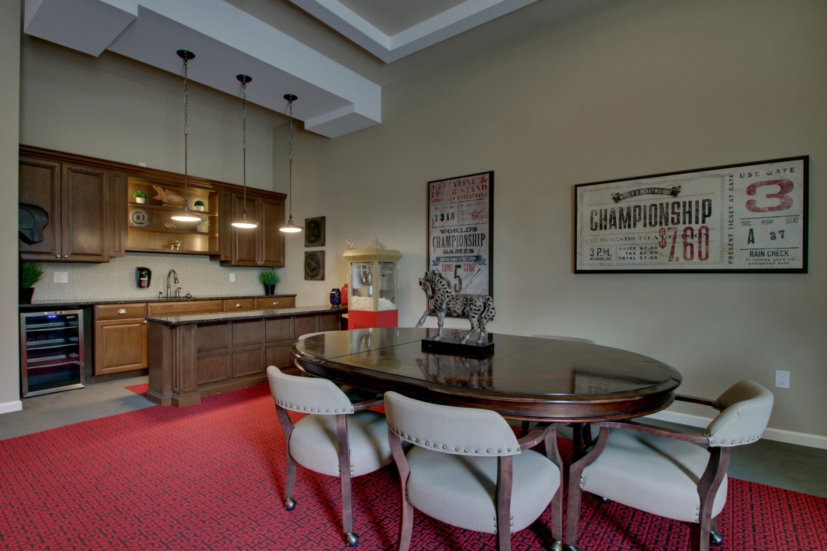 A modern dining area with a wooden table, upholstered chairs, and an open kitchen featuring pendant lighting and wooden cabinetry.