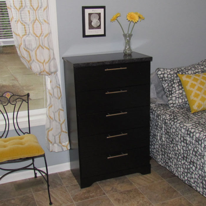 A cozy room with a black dresser, yellow chair, floral vase, and patterned sofa.