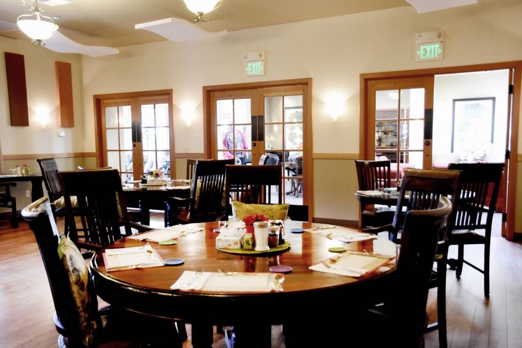 An empty dining room with neatly set tables and chairs, featuring large windows.