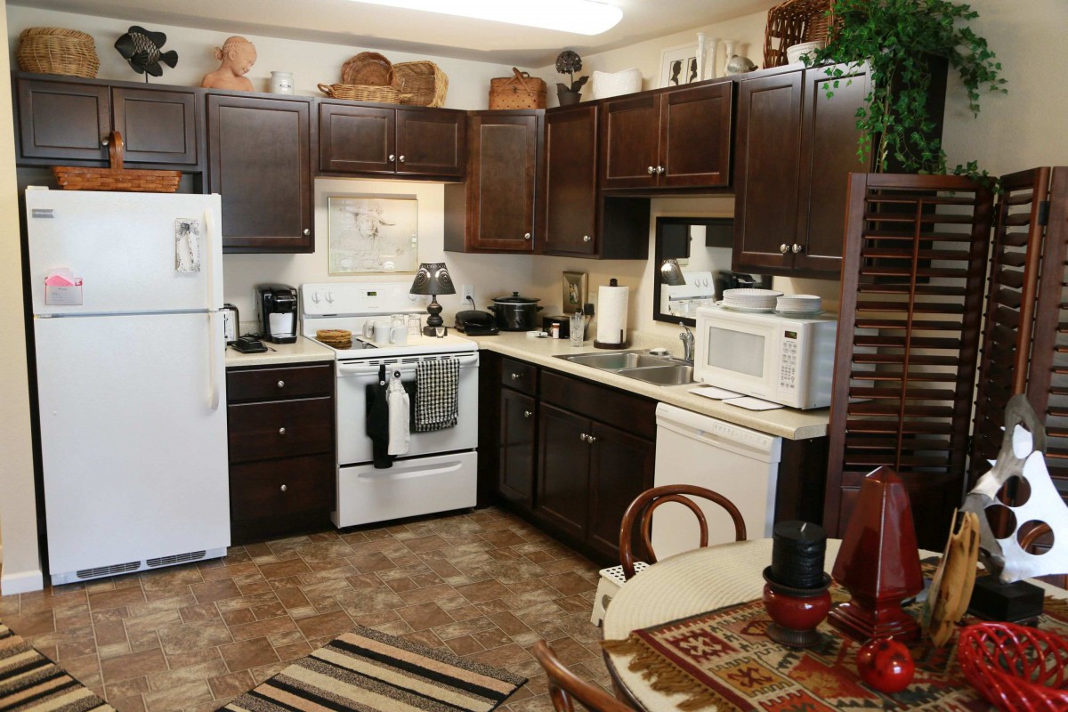 A cozy kitchen with dark cabinets, a stove, microwave, refrigerator, and various appliances.