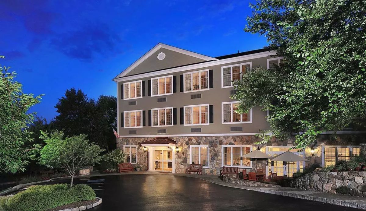 A well-lit hotel exterior at night with surrounding trees.