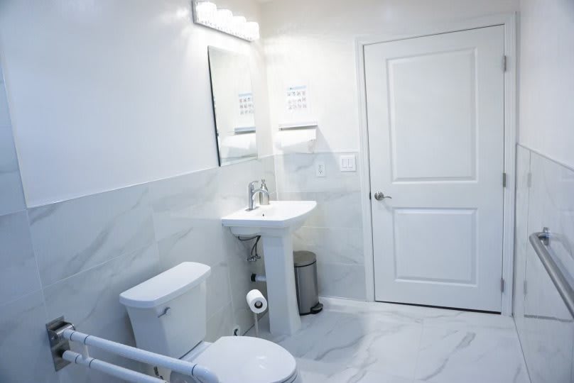 A clean and minimalist bathroom with white tiles, featuring a sink, toilet, and towel dispenser.