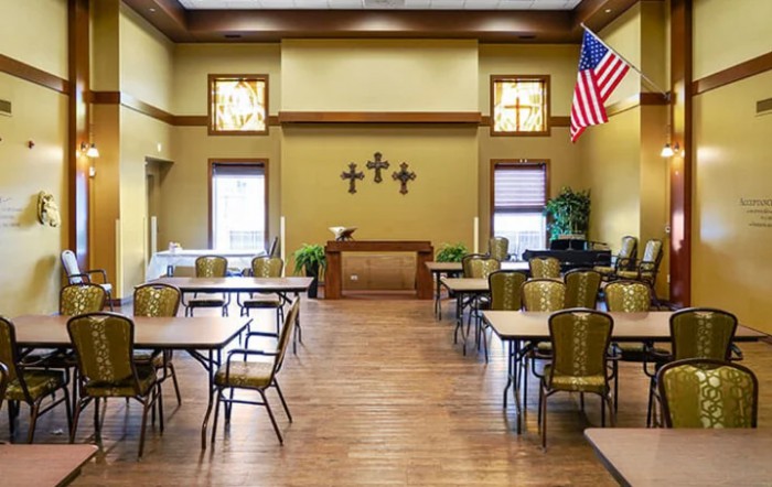 A quiet room with tables and chairs, featuring a prominent display of crosses on the wall and an American flag.