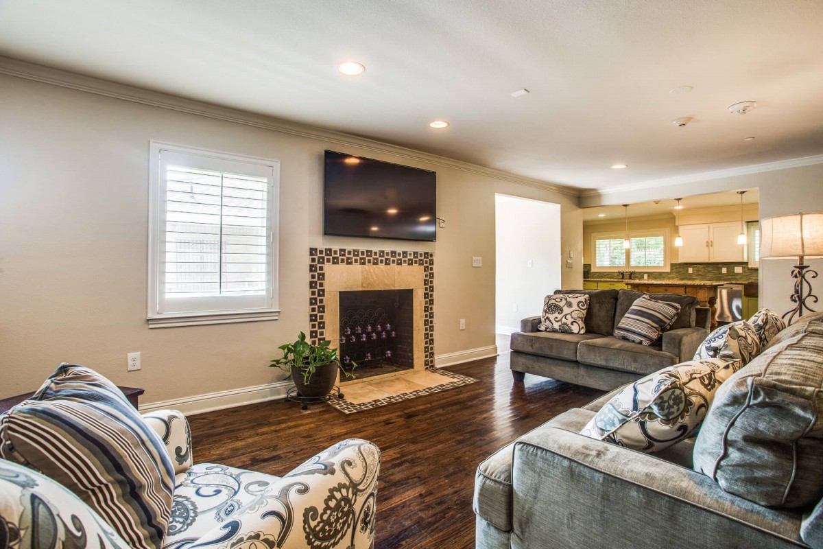 A cozy living room featuring a fireplace with a mounted TV above, hardwood floors, and comfortable sofas.
