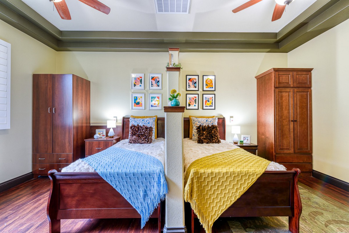 A well-decorated bedroom featuring twin beds with colorful quilts and matching wooden furniture, complemented by artwork on the walls.