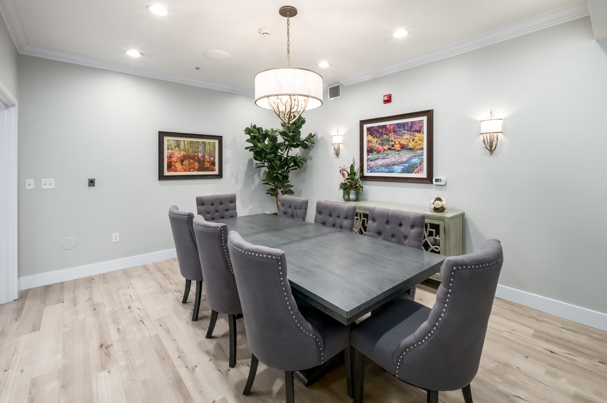 A modern dining room with a sleek table and upholstered chairs, illuminated by a chandelier and adorned with artwork.