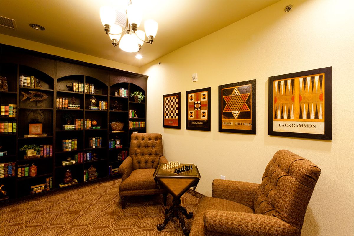 A cozy library with comfortable armchairs, bookshelves, and artwork depicting board games.