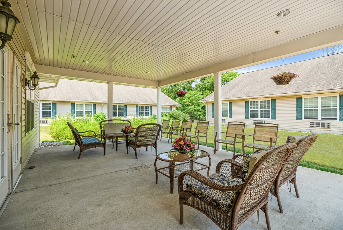A cozy patio with wicker chairs and tables under a covered area, surrounded by green foliage.