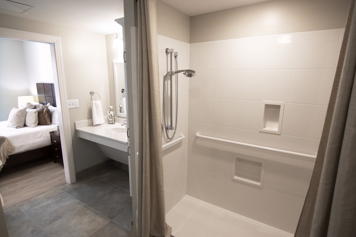 A modern, accessible bathroom with a shower equipped with handrails and a sink with a mirror.