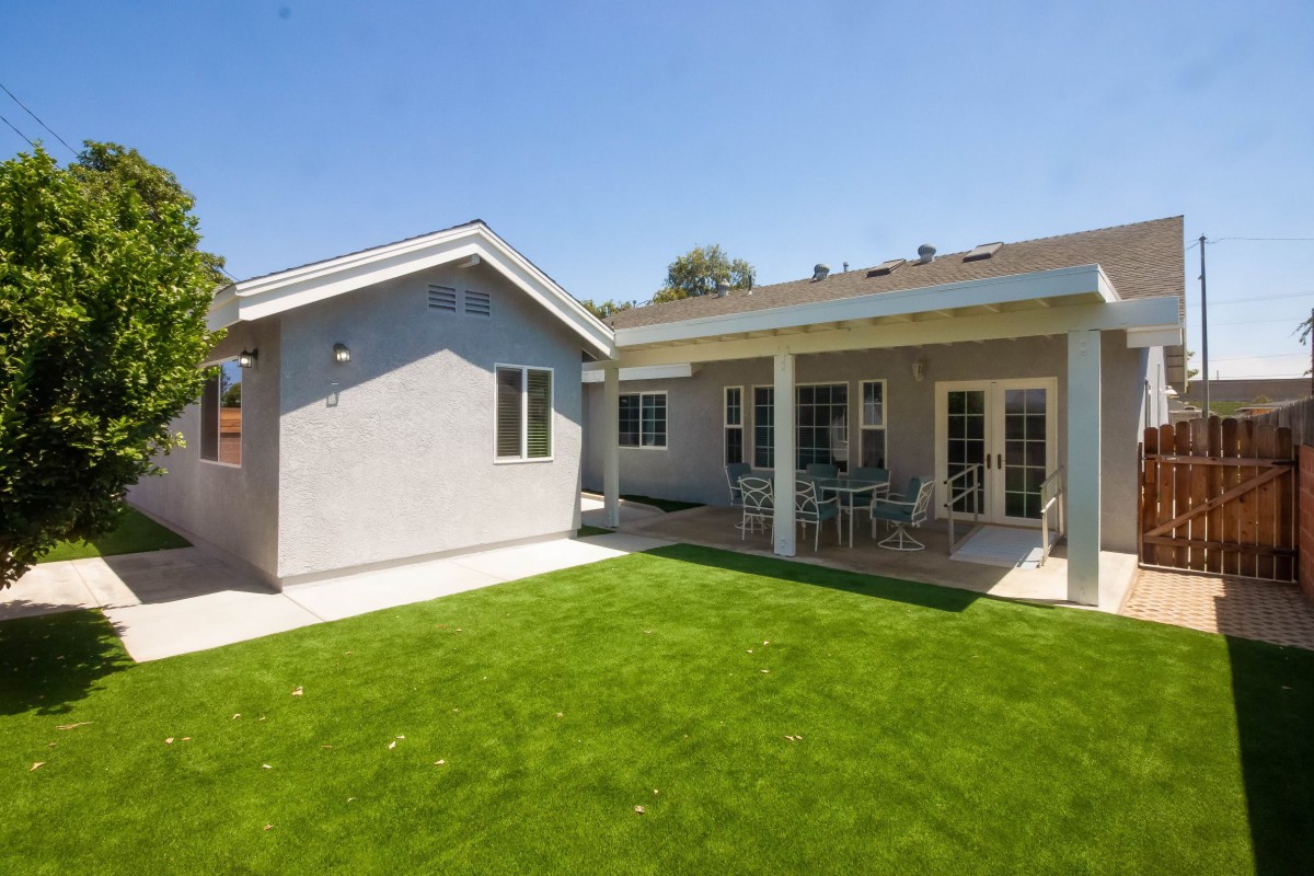 A sunny view of a house with a well-maintained backyard and patio area.