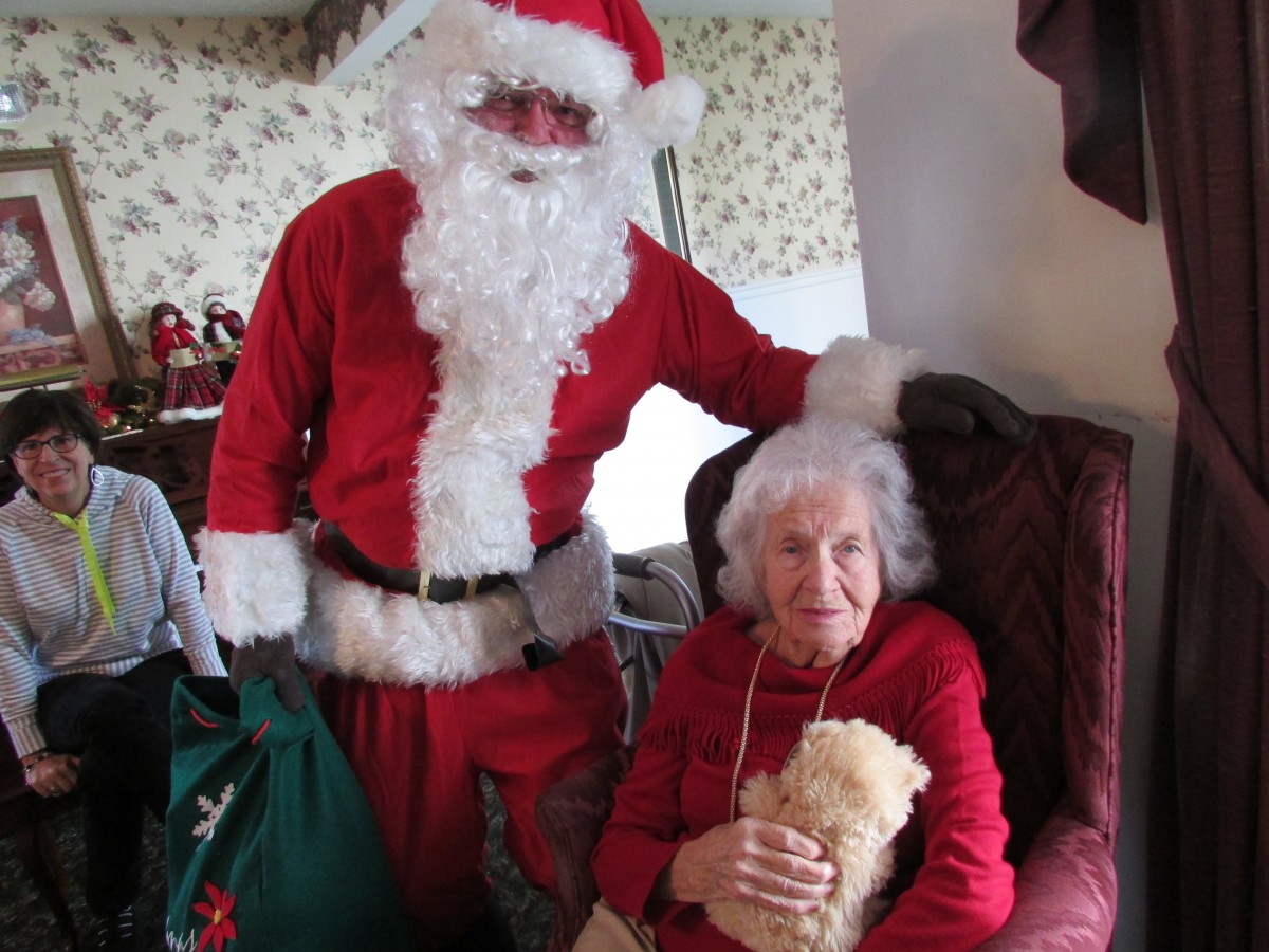 A person dressed as Santa Claus stands next to an elderly woman during a holiday celebration.