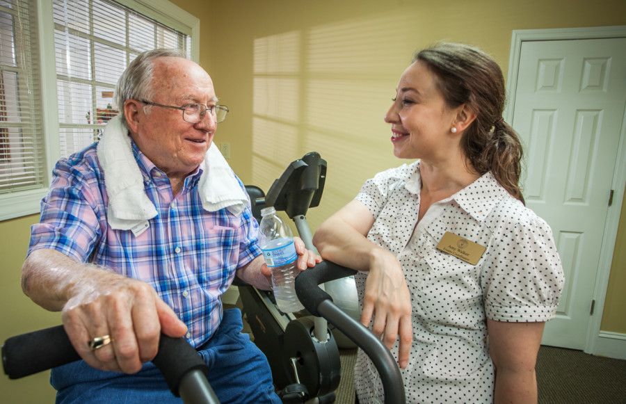 An elderly man talking with a healthcare professional while using fitness equipment.