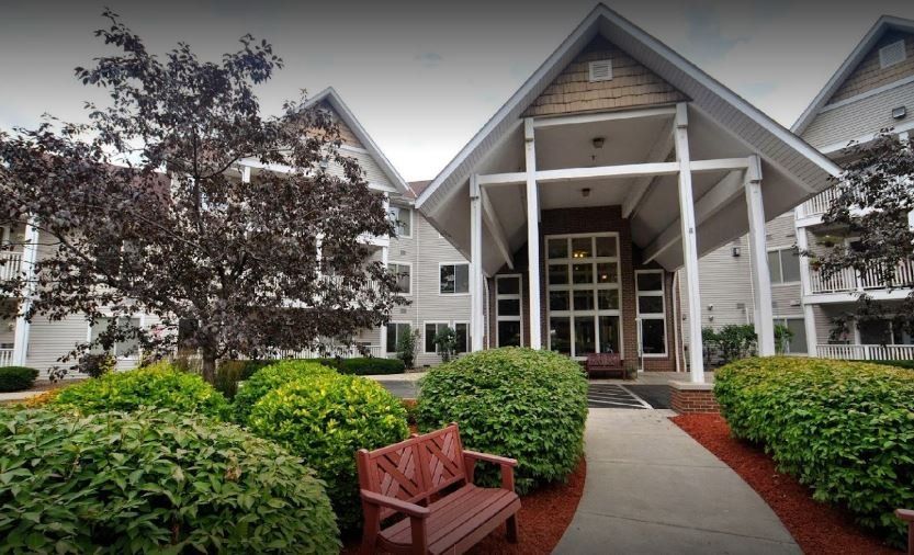 A charming building entrance with manicured landscaping and a wooden bench.