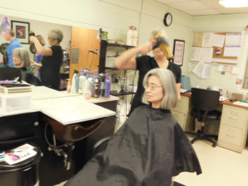 A hairstylist works on a client's hair in a busy salon.