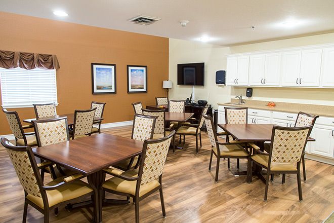 A cozy dining room with several tables and chairs, featuring a kitchen area and wooden floors.