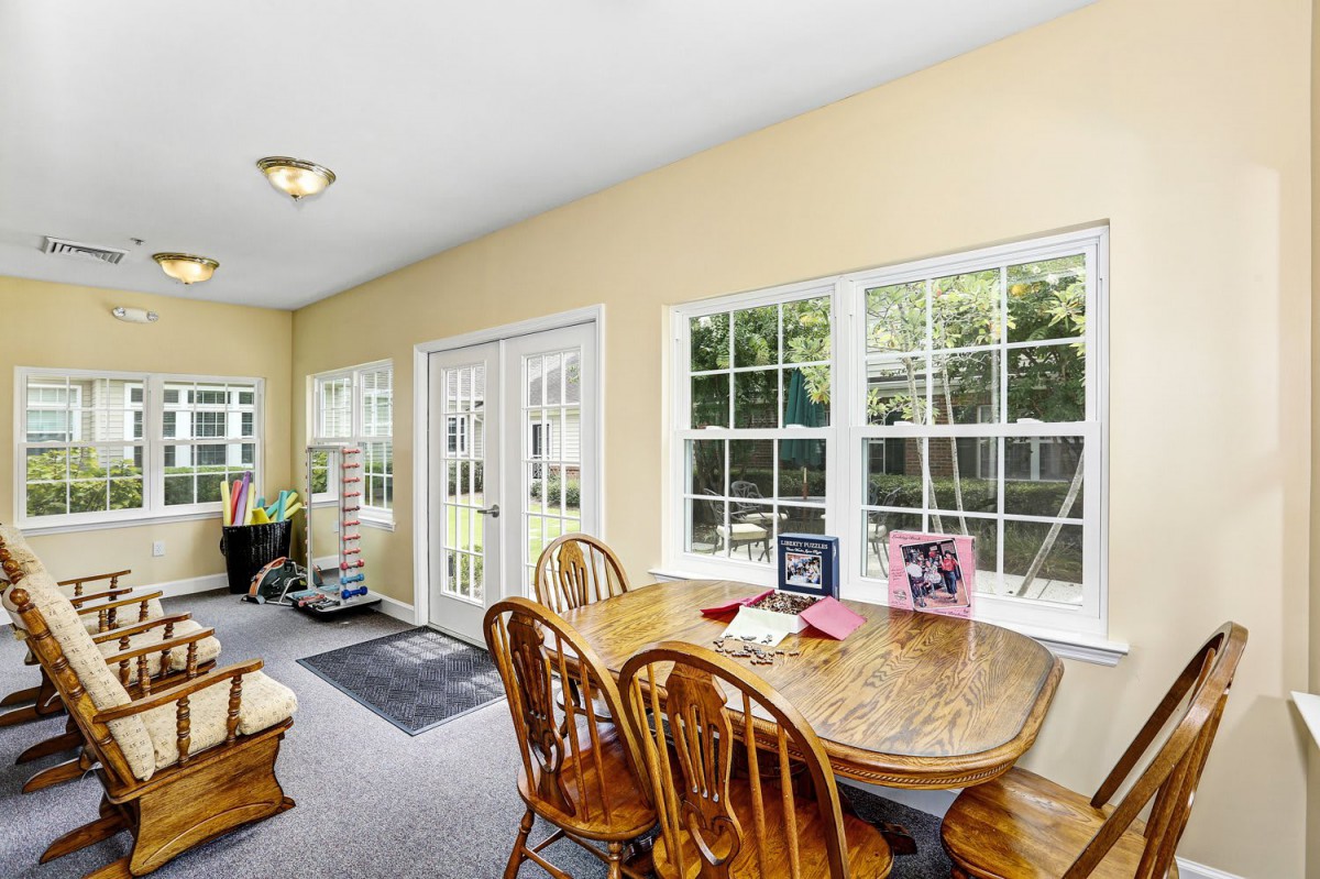 A bright dining area featuring a wooden table and chairs, surrounded by large windows that flood the space with natural light.