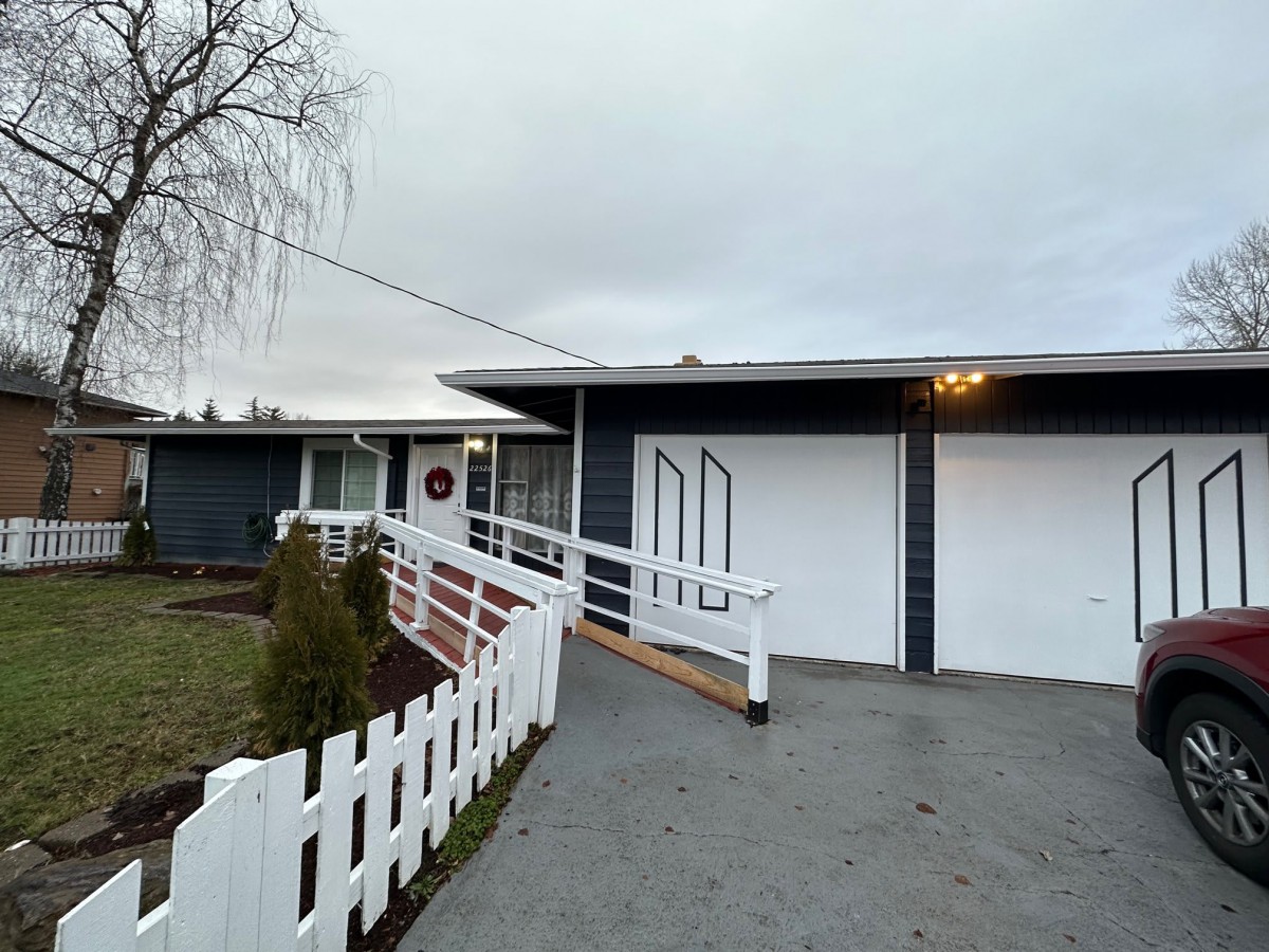 A suburban house with a ramp leading to the front entrance, featuring a white fence and garage.
