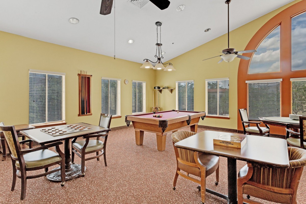 A cozy game room featuring a pool table and chess board, complemented by natural light from multiple windows.