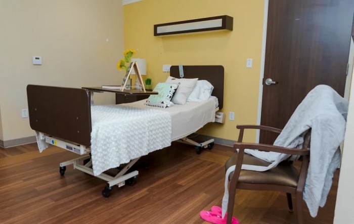 A well-organized hospital room featuring a single bed, a chair, and medical equipment.