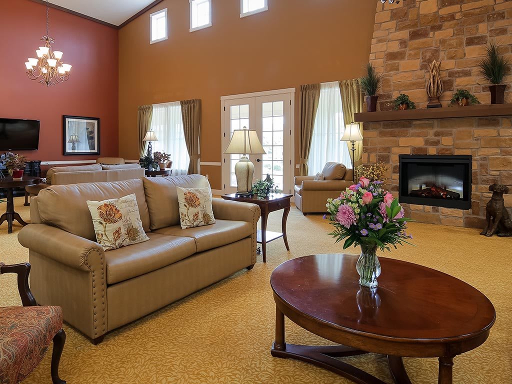 A cozy living room featuring a sofa, coffee table with flowers, and a warm fireplace.