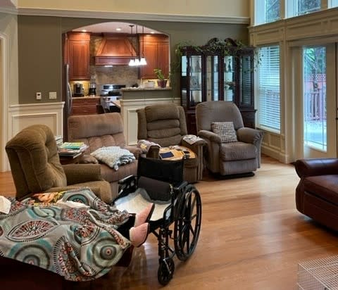 A cozy living room with armchairs, a couch, and a wheelchair near large windows.