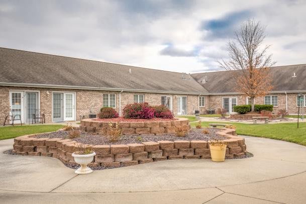A brick residential building with a landscaped courtyard featuring flowerbeds and potted plants.