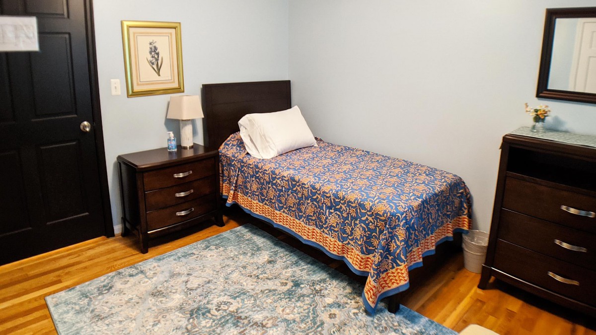 A cozy bedroom with a single bed, nightstand, and decorative rug.