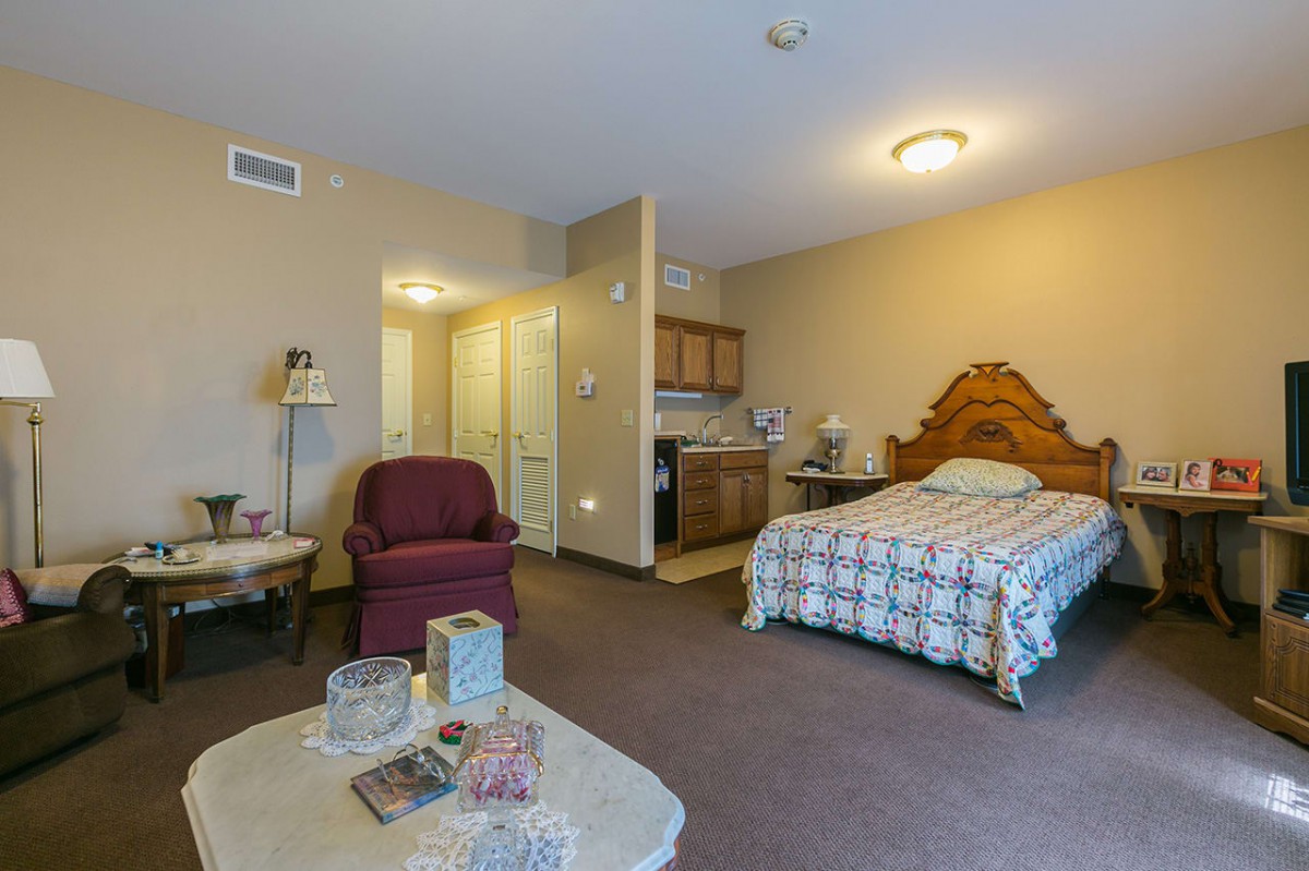 A cozy studio apartment featuring a bed, armchair, and a small kitchenette.