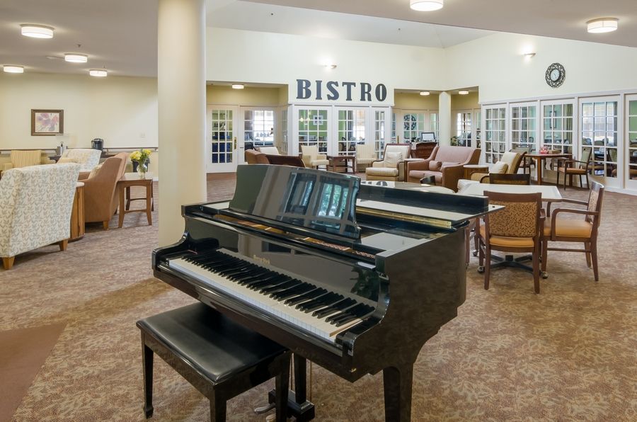A grand piano in a bistro setting with tables and chairs.