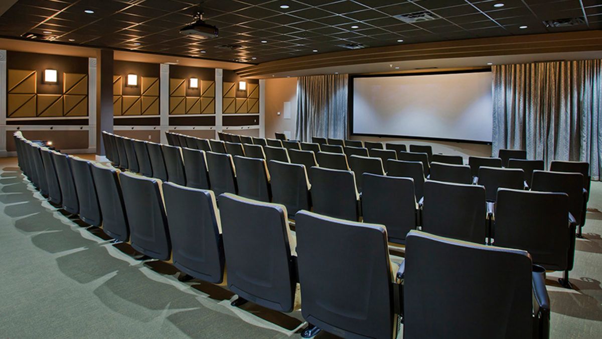 Empty theater room with arranged seating facing a large projection screen.