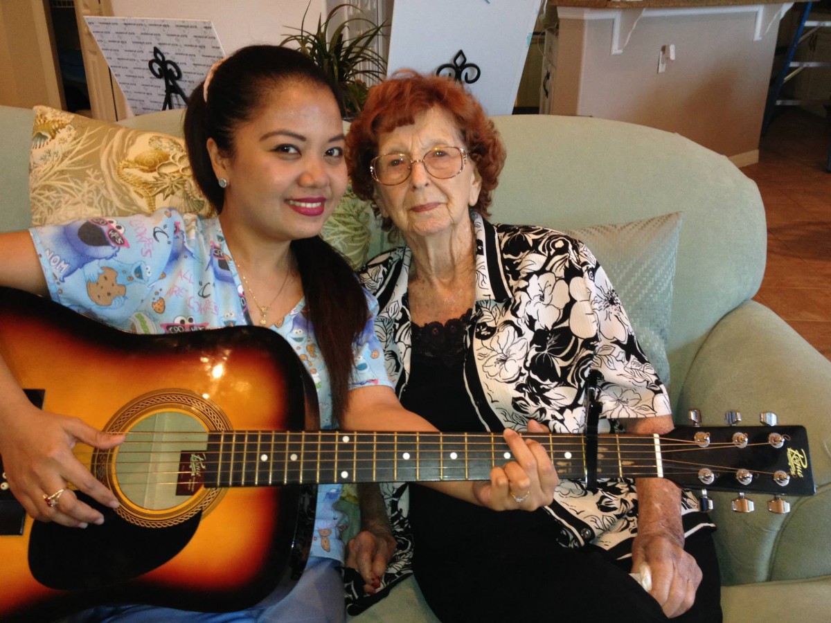 Two women sitting indoors, smiling with a guitar.