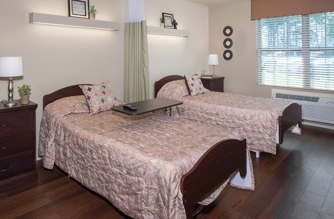 A cozy nursing home room with two beds and tasteful decor.