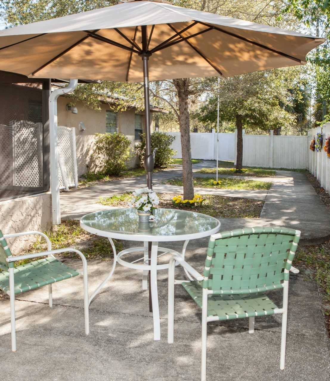 A peaceful backyard patio setup with a glass table, chairs, and an umbrella.