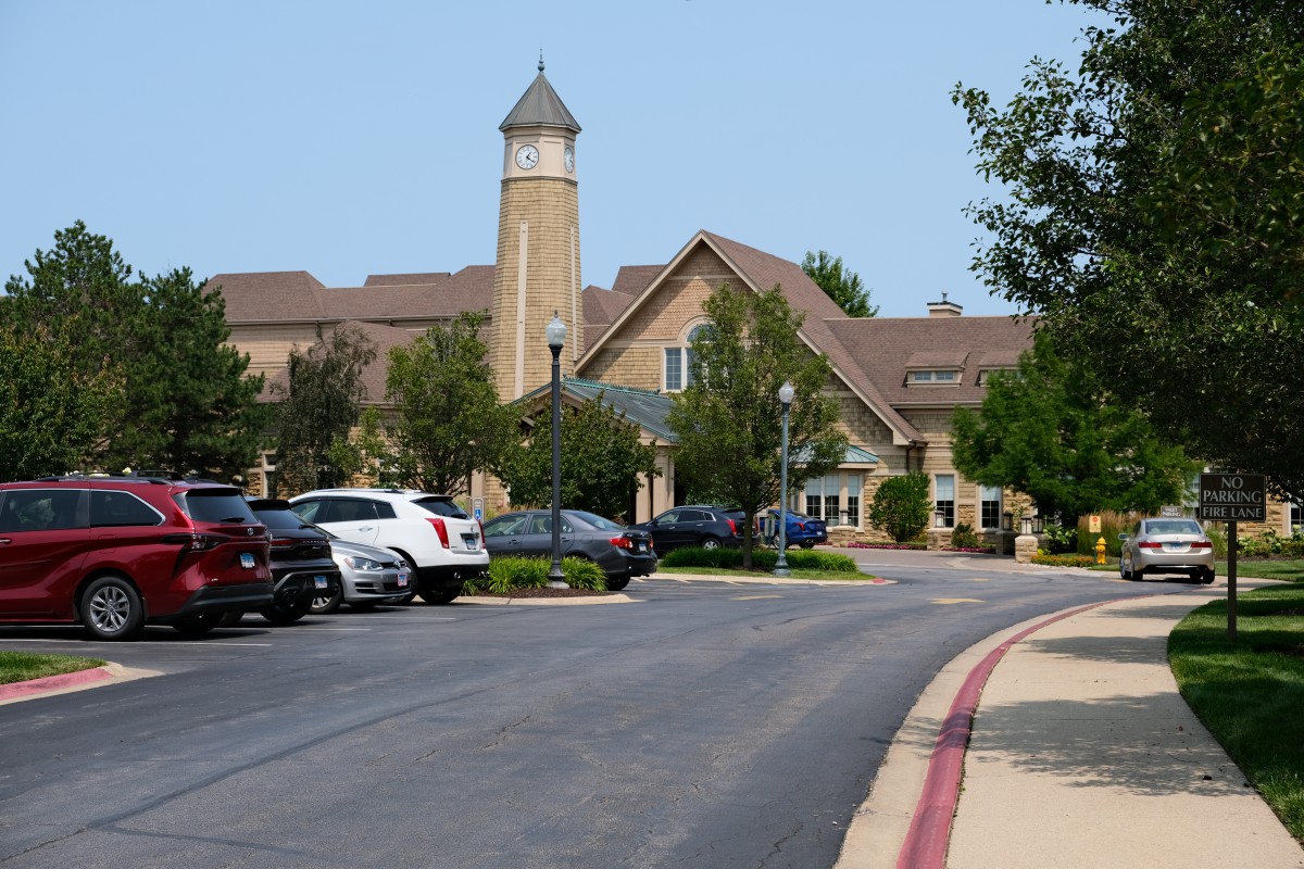A scenic view of a building with a clock tower, surrounded by parked cars and greenery.