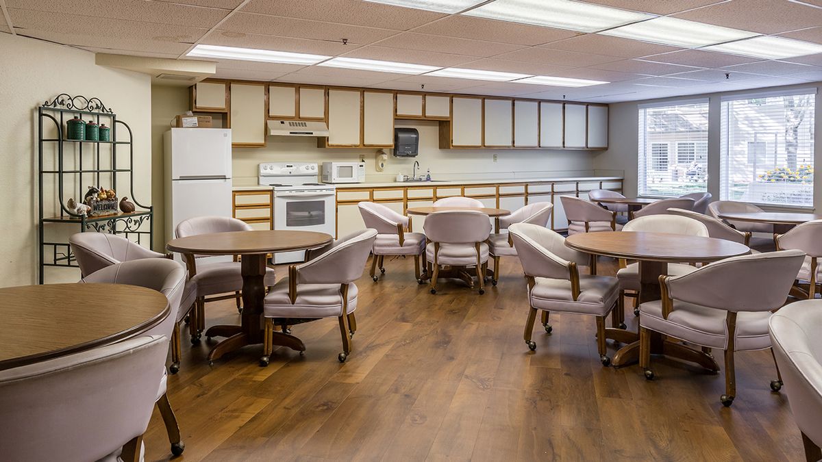 A communal kitchen and dining area featuring several round tables with chairs, surrounded by cabinetry and appliances.