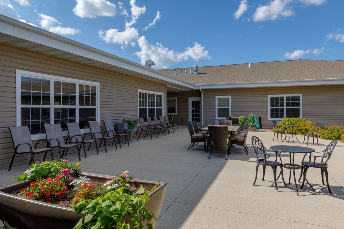 An outdoor patio area with tables and chairs, surrounded by plants under a clear blue sky.