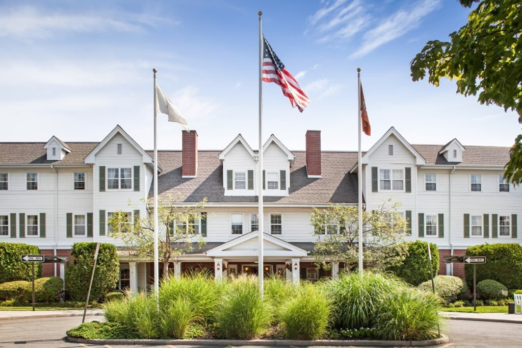 A large white building with multiple flags in front, surrounded by well-maintained landscaping and set against a clear sky.