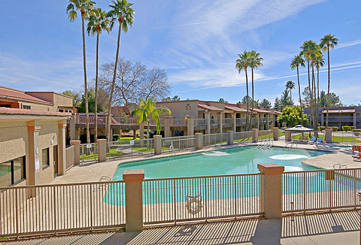A serene view of an apartment complex featuring a sparkling swimming pool surrounded by palm trees.