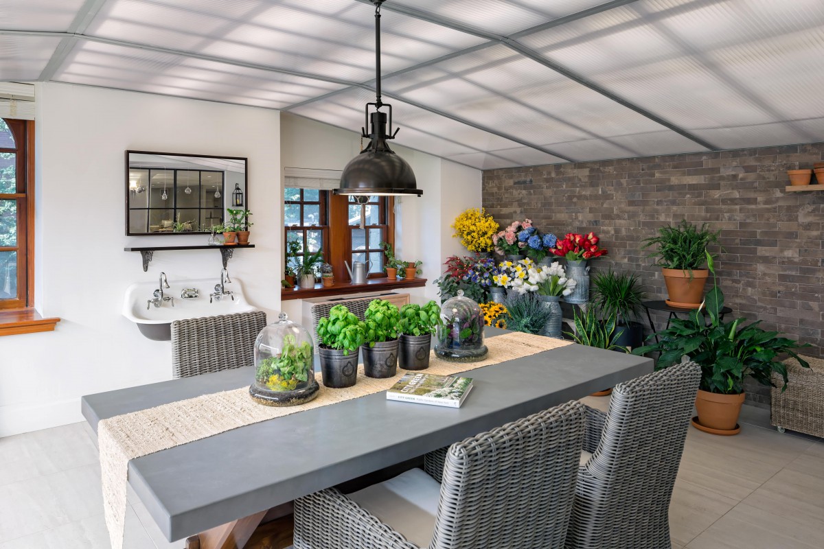 A modern dining room with indoor plants and flowers, featuring wicker chairs and a pendant light.