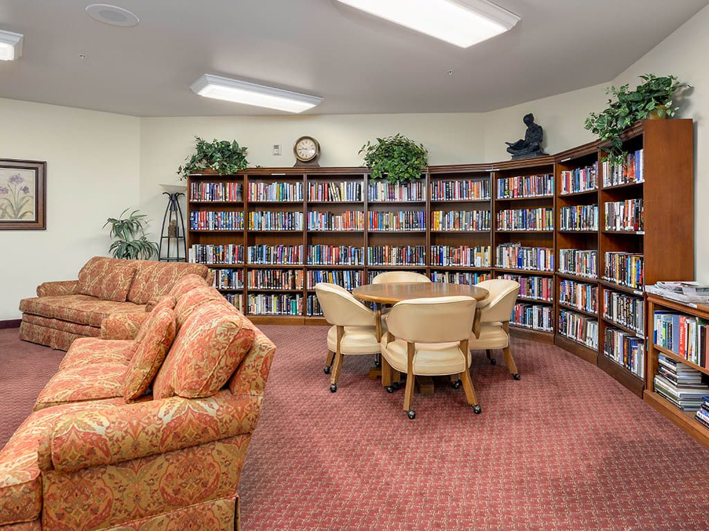 A cozy library room with a round table, chairs, and a sofa surrounded by bookshelves.