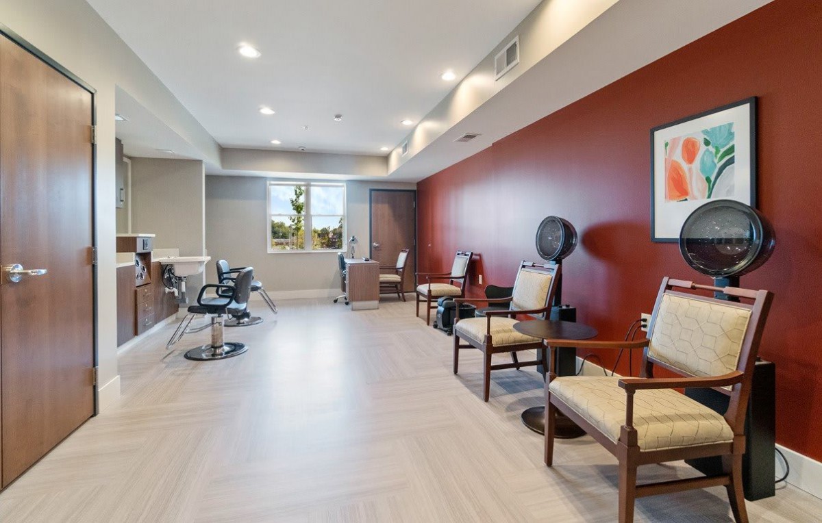 A modern salon interior featuring a waiting area with chairs and a red accent wall.
