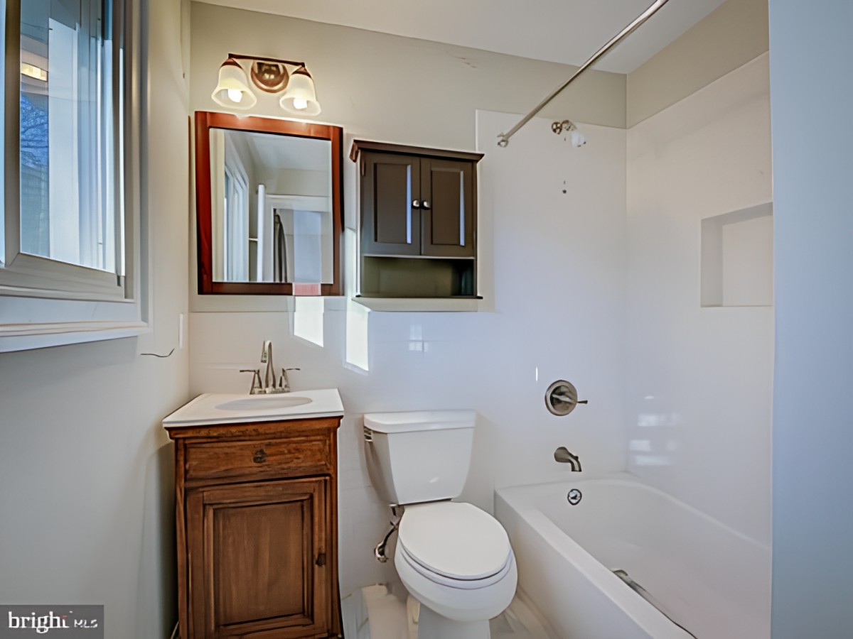 A small bathroom with a bathtub, toilet, and wooden vanity.