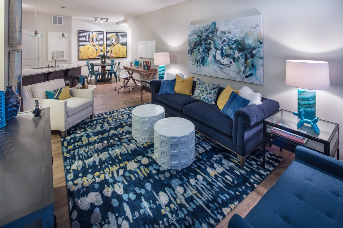 A stylish living room featuring a modern blue color scheme with artwork, a plush sofa, patterned rug, and white coffee tables.