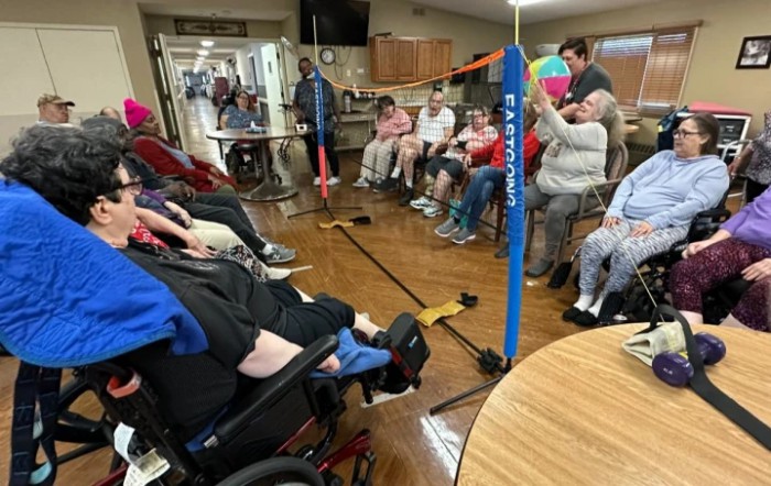 A group of seniors participating in an indoor community activity, with several individuals seated in wheelchairs.