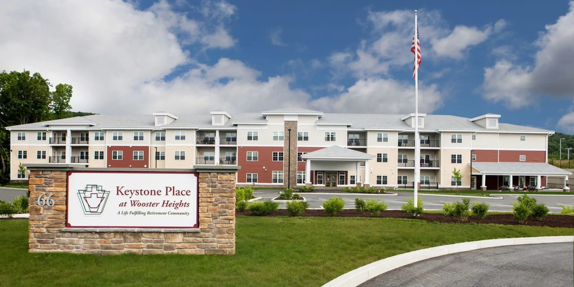 A modern residential building with a well-maintained lawn and a sign at the entrance, set against a partly cloudy sky.