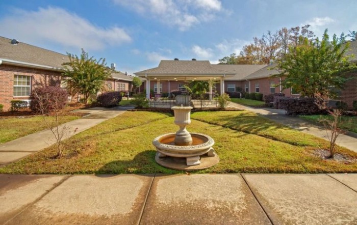 A tranquil courtyard featuring a central fountain and a gazebo surrounded by well-manicured lawns under a clear blue sky.