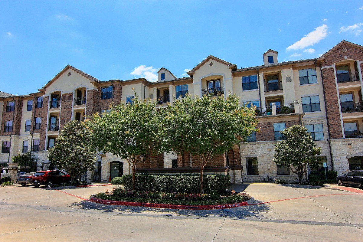 A multi-story residential building with trees in the foreground under a clear blue sky.