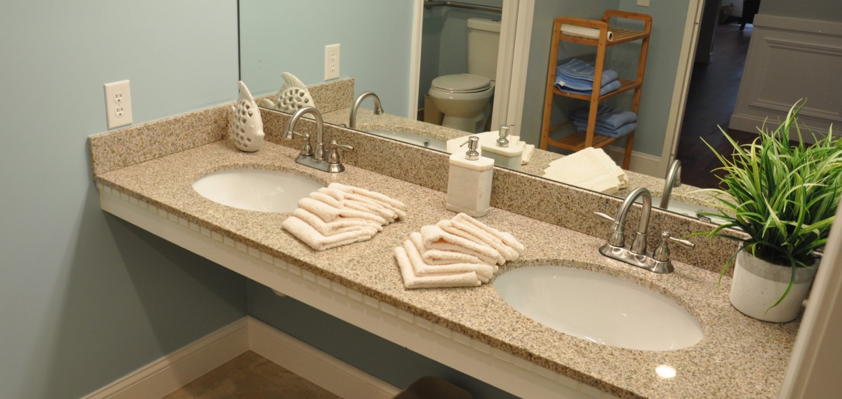 A neatly organized bathroom with a double sink and folded towels on a granite countertop.