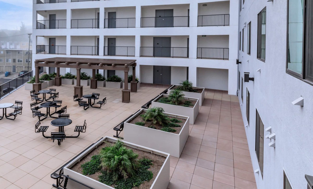 A view of a hotel courtyard with outdoor seating and planters, surrounded by balconies.